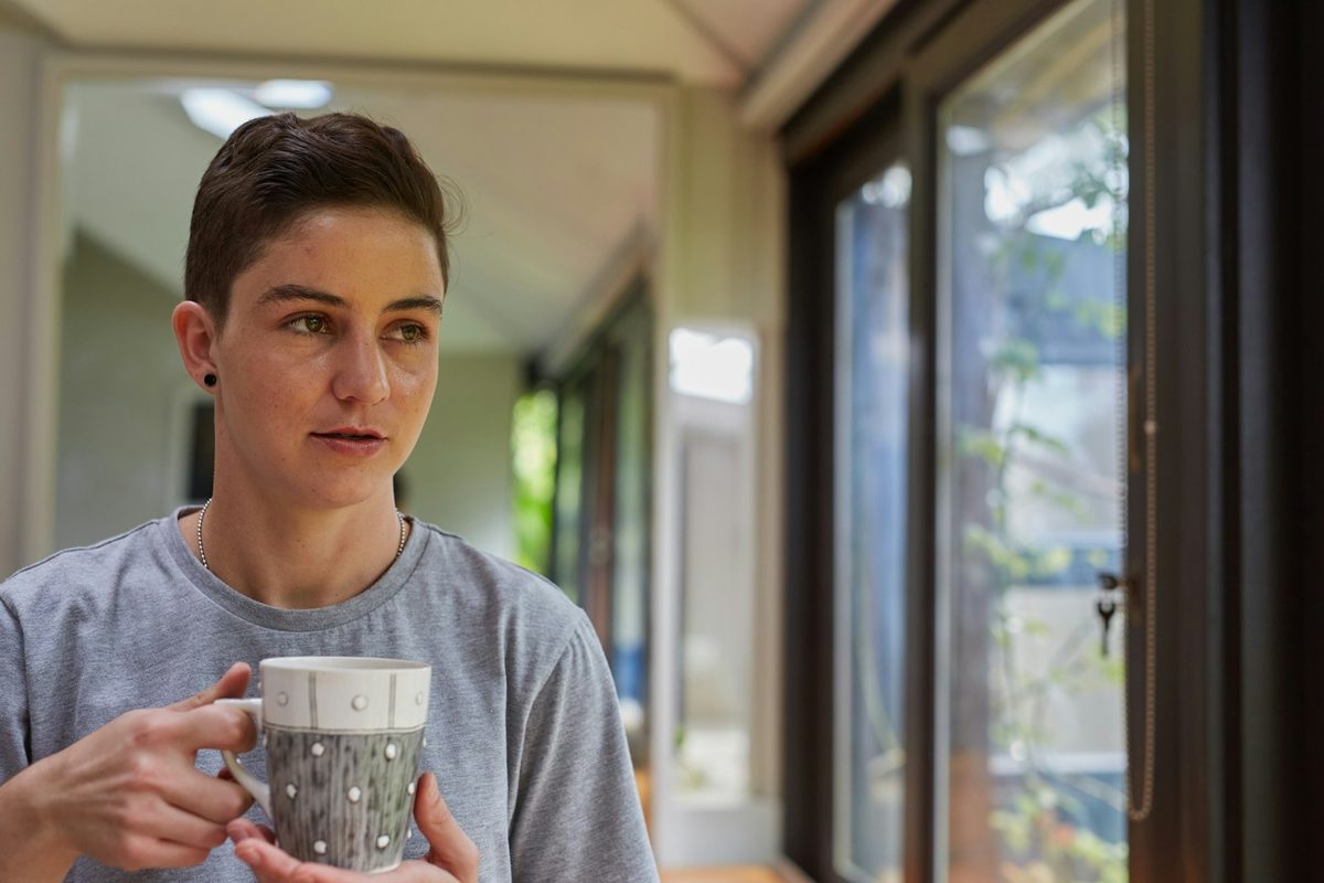 Ettertenksom person med kaffekopp ved vinduet i rolig dagslys