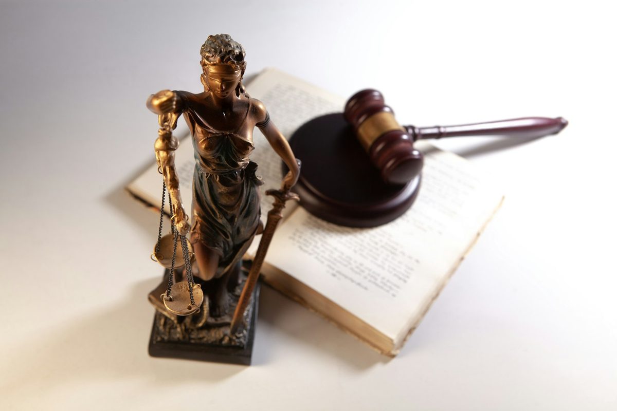 Justitia-statue med skålvekt ved dommerklubbe og oppslått lovbok